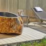 Steinbadewanne und Liegestühle auf Holzterrasse im Freien.