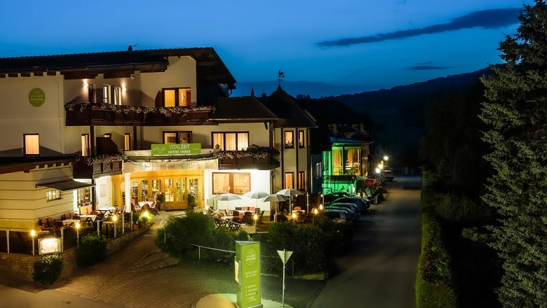 Vitalzeit Hotel Weber, © Michael-Giefing Außenansicht des Vitalzeit Hotel Weber bei Nacht, beleuchtet mit warmem Licht, umgeben von Bäumen und geparkten Autos.