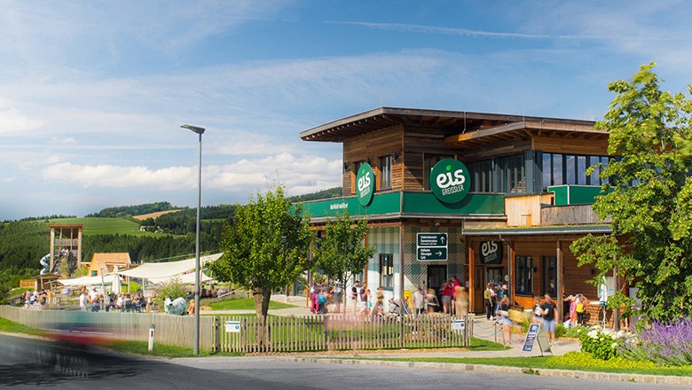 Gebäude der Eis-Greissler Welt mit Bäumen und Besuchern und Blick auf den Erlebnispark.
