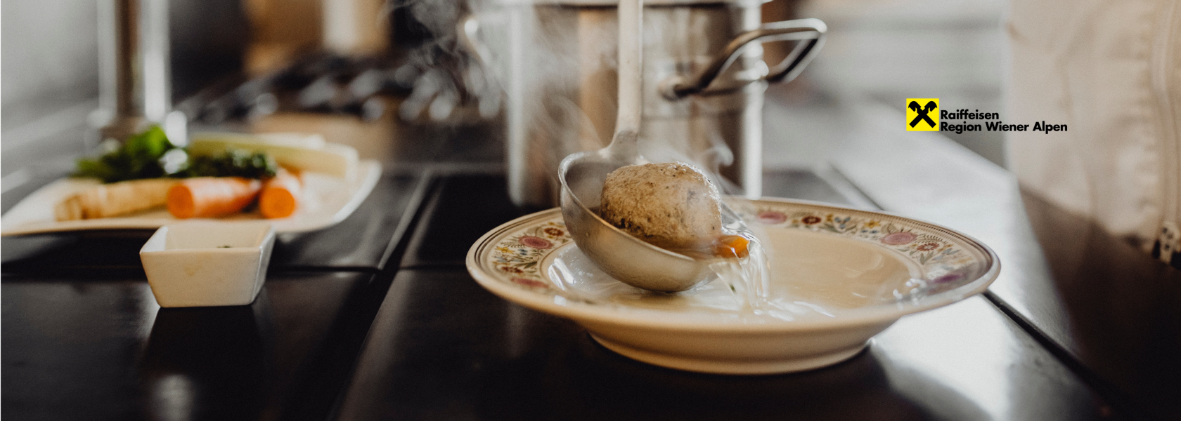 Suppe und ein Knödel werden mit einer Kelle in ein Suppenteller gegossen und Dampf steigt auf.