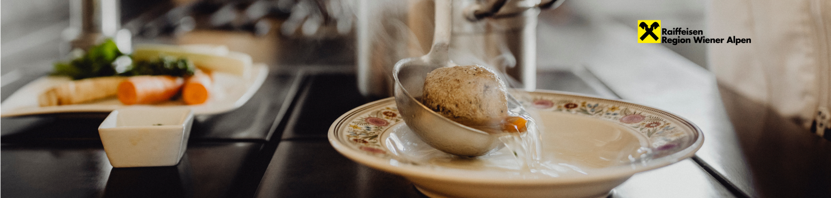 Suppe und ein Knödel werden mit einer Kelle in ein Suppenteller gegossen und Dampf steigt auf.