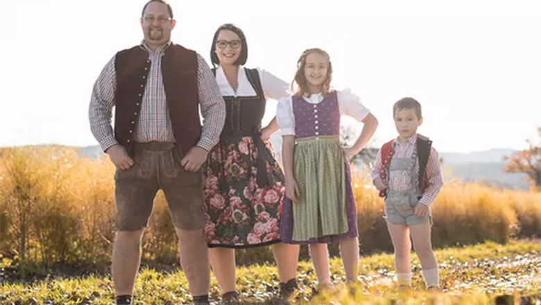 Eine Familie mit zwei Kindern in Tracht gekleidet steht auf einem Weg vor einem Feld.