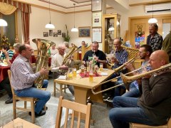 Gruppe von Männern spielt Blasinstrumente in einer gemütlichen Gaststube.