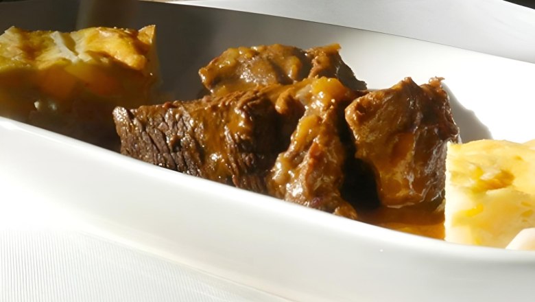 Tiefer, weißer Teller mit geschmortem Wildschweinbraten und Beilagen.