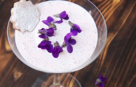 Glas mit Veilchen-Creme, Veilchenblüten und Mürbteigkeks auf rustikalem Holztisch.