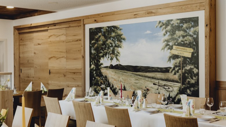 Innenansicht eines Wirtshauses mit gedecktem Tisch und Wandgemälde.