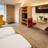 Modern eingerichtetes Hotelzimmer mit gelbem Sessel, Holzmöbeln und Blumen auf einem Tisch.