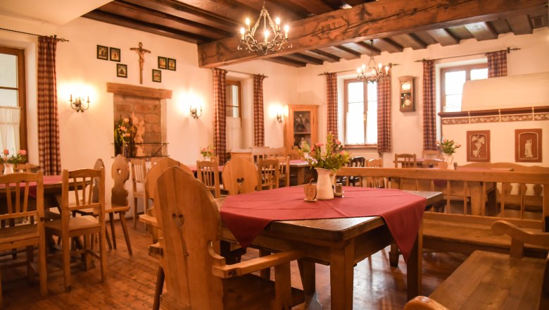 Gem&uuml;tliche Stube mit Holzm&ouml;beln, roten Tischdecken und Kronleuchtern.