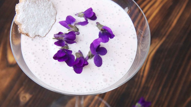 Glas mit Veilchen-Creme, Veilchenblüten und Mürbteigkeks auf rustikalem Holztisch.